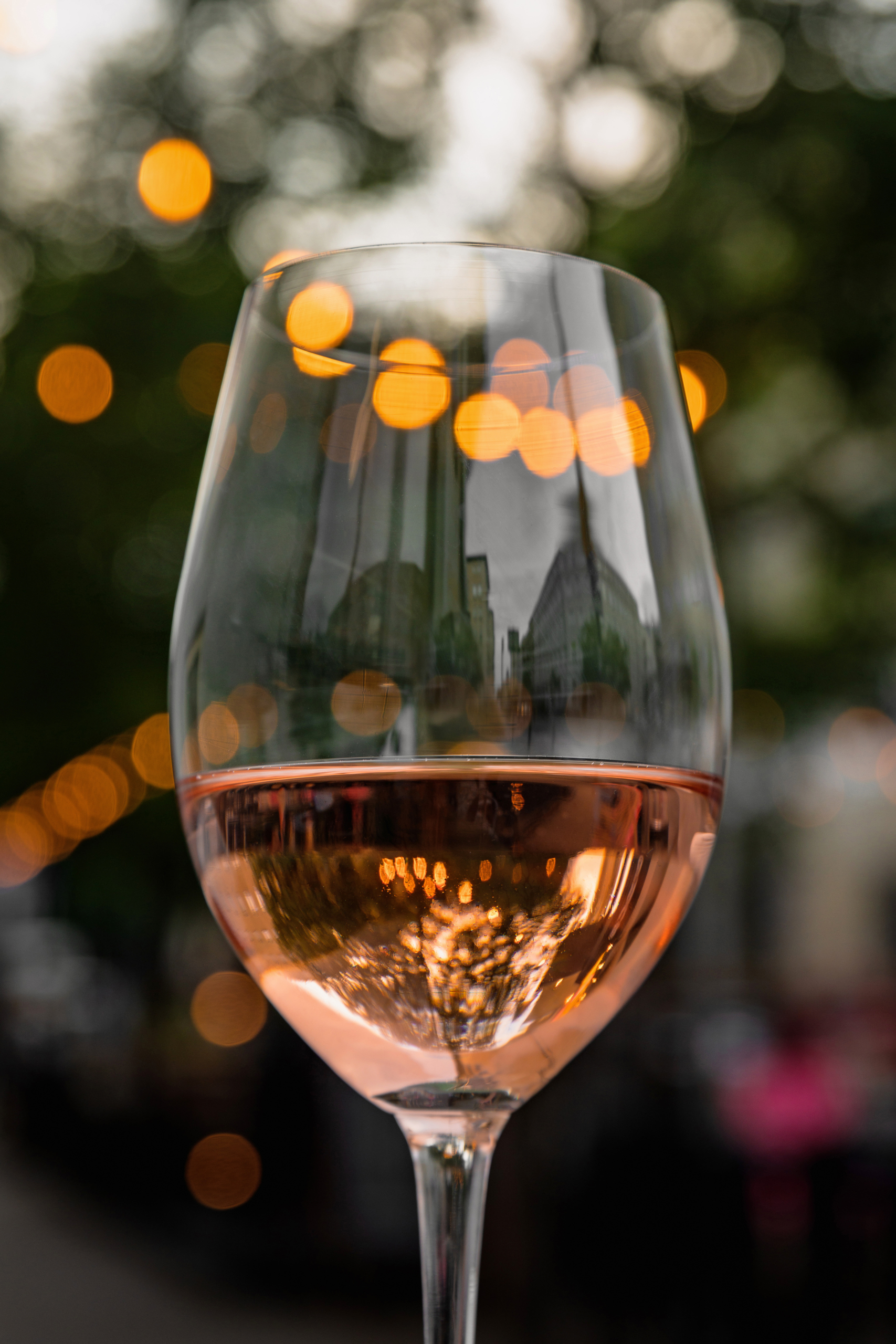 Close-up of a glass of refreshing rose wine on the green table of a city cafe terrace during warm summer evening. Street in bokeh.